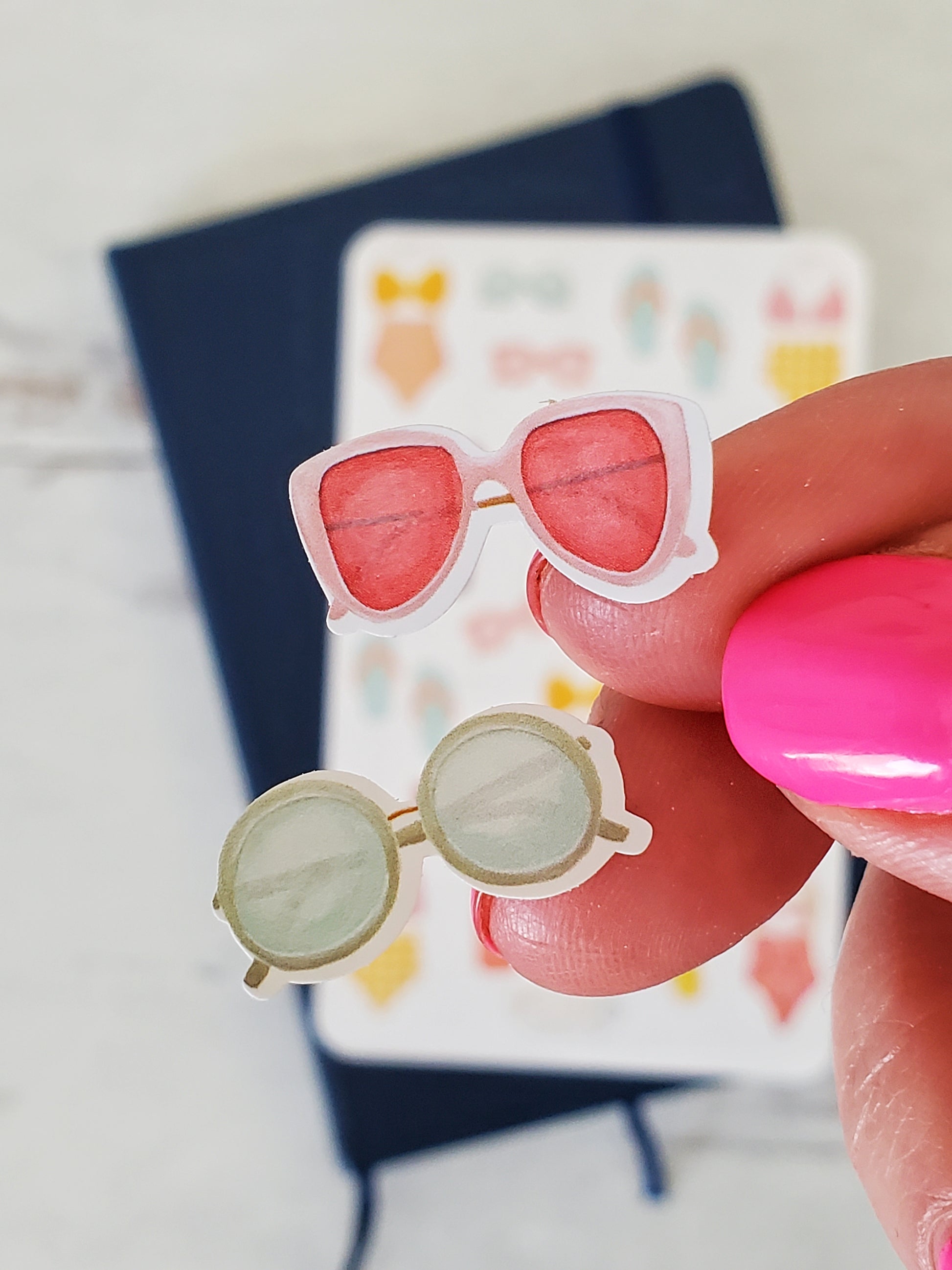 Close up of two different sunglasses stickers, one is pink aviator sunglasses the other is round green sunglasses.