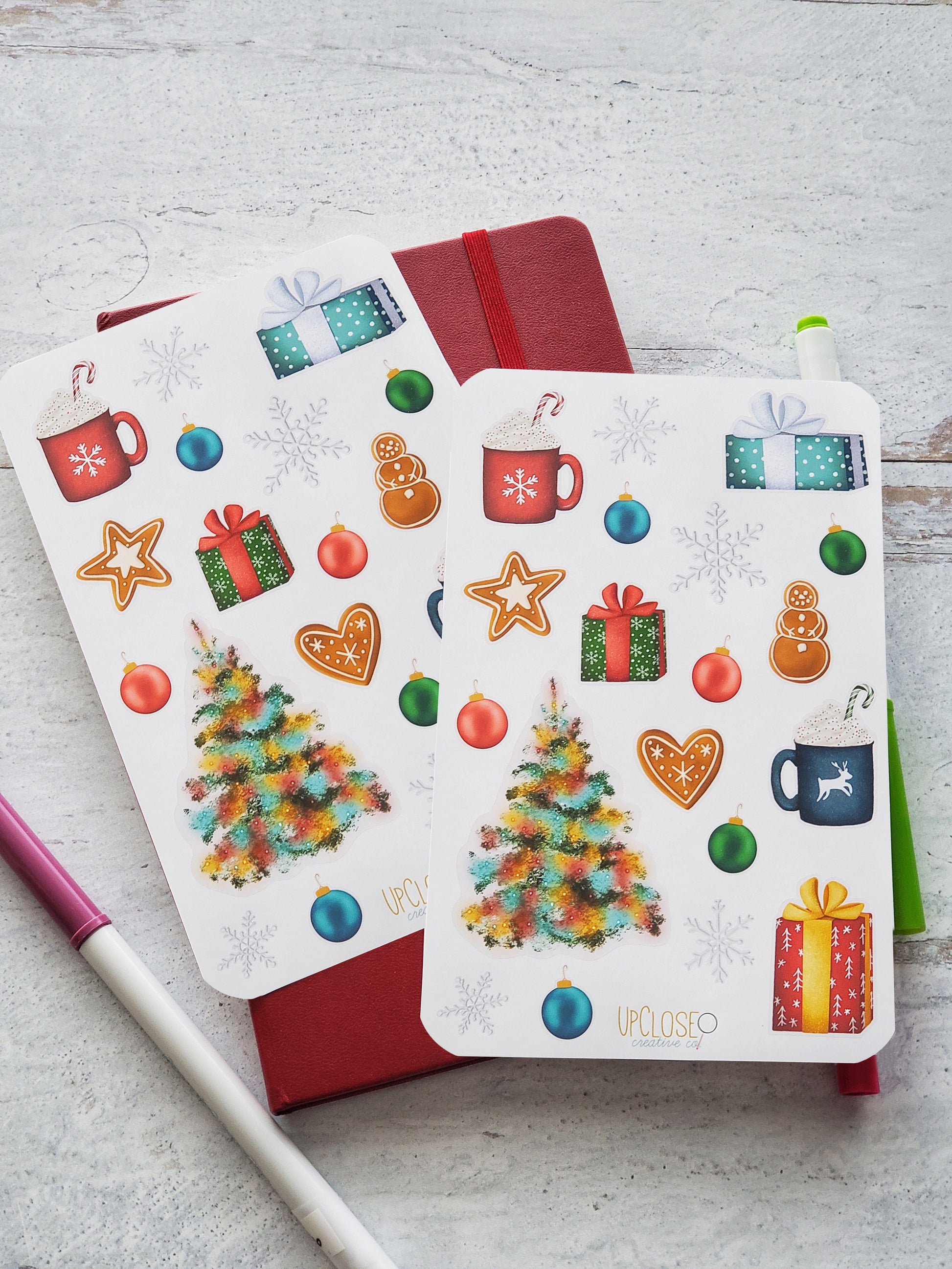 Set of two sticker sheets featuring illustrated Christmas icons including a tree with colorful lights, gingerbread cookies, hot cocoa mugs with whipped cream, ornaments, wrapped gifts and snowflakes. 