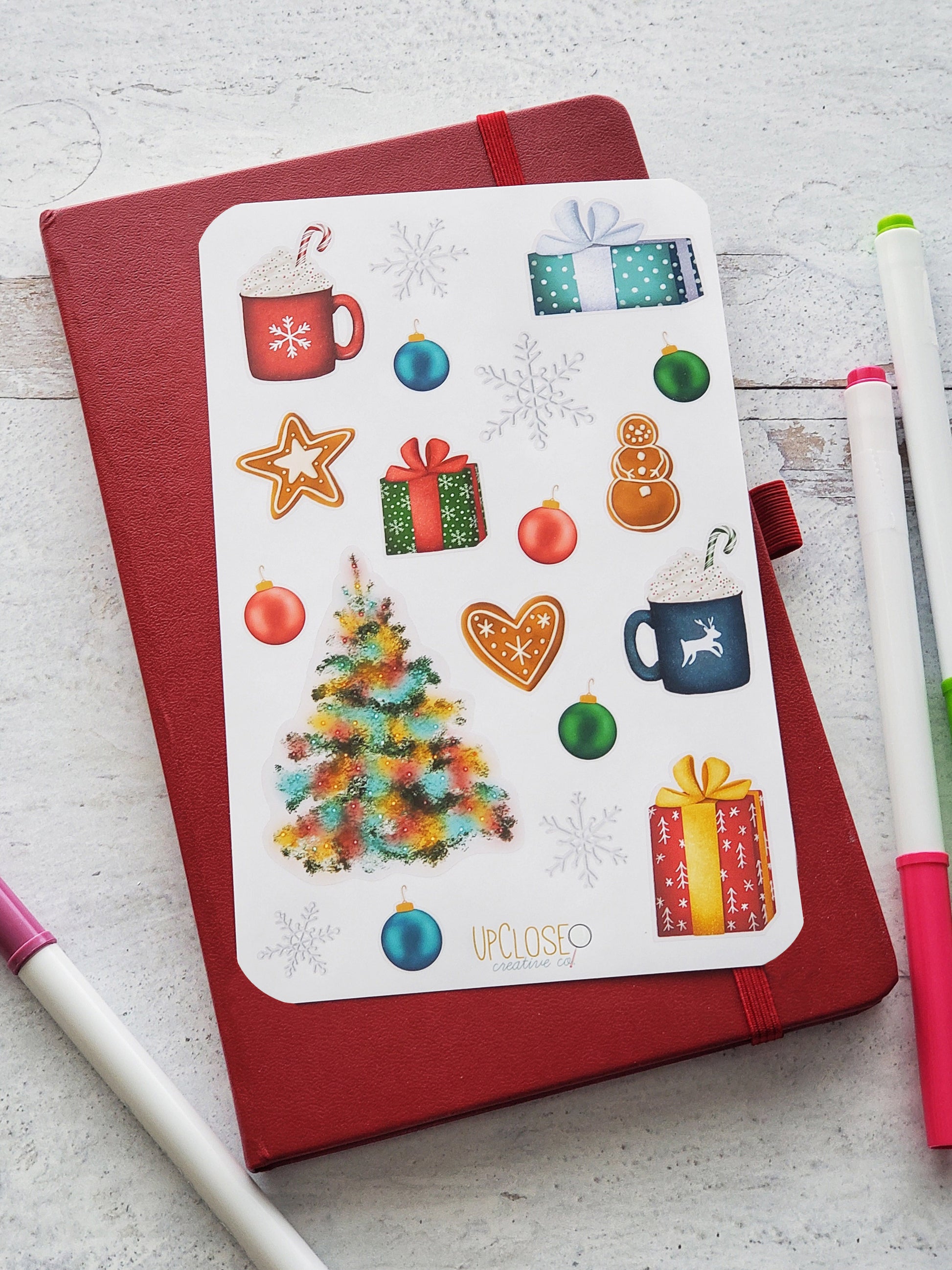 Sticker sheet featuring illustrated Christmas icons including a tree with colorful lights, gingerbread cookies, hot cocoa mugs with whipped cream, ornaments, wrapped gifts and snowflakes. 