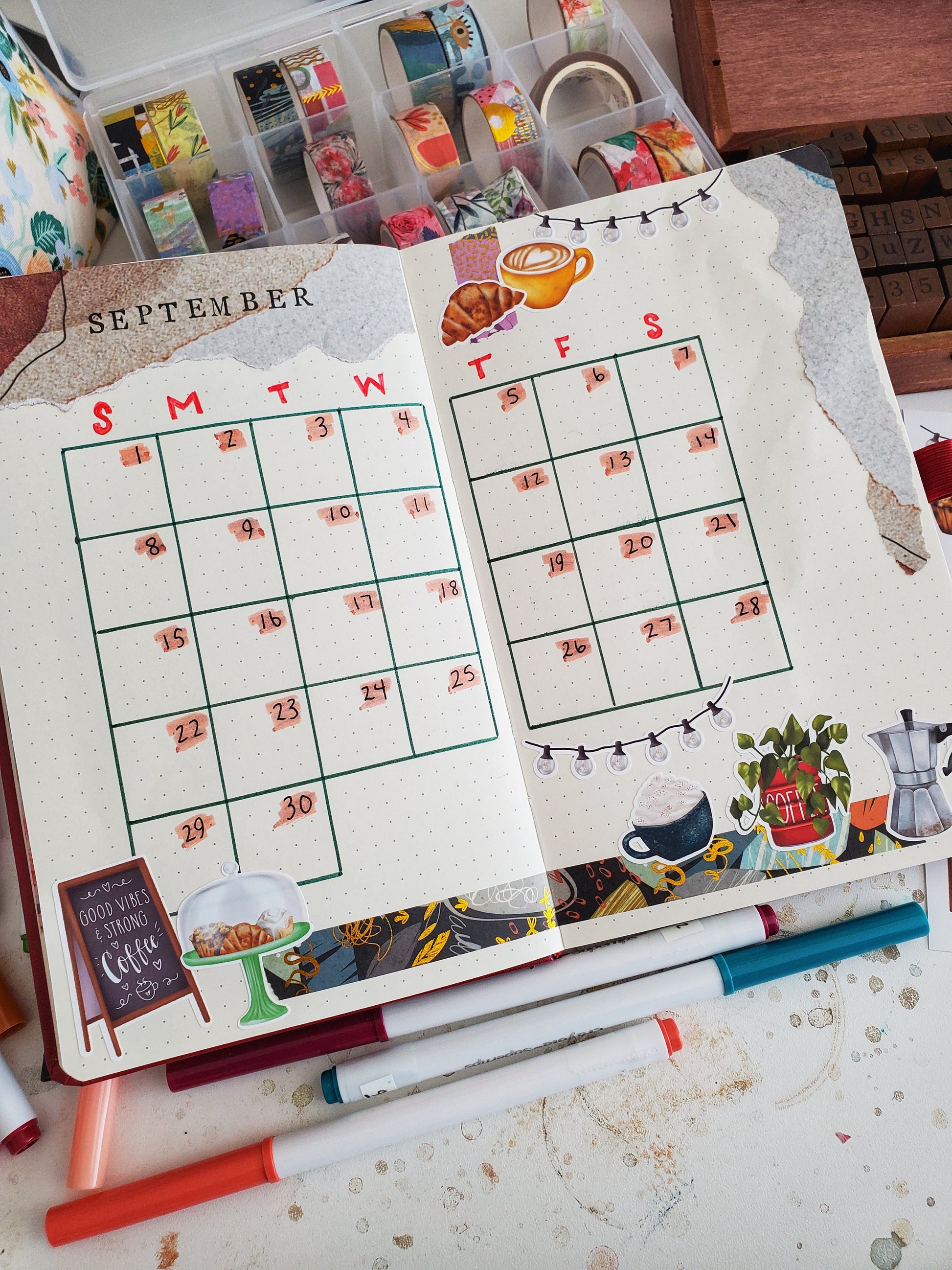 A bullet journal open to a calendar spread decorated with stickers from the eclectic coffee shop sticker sheet.