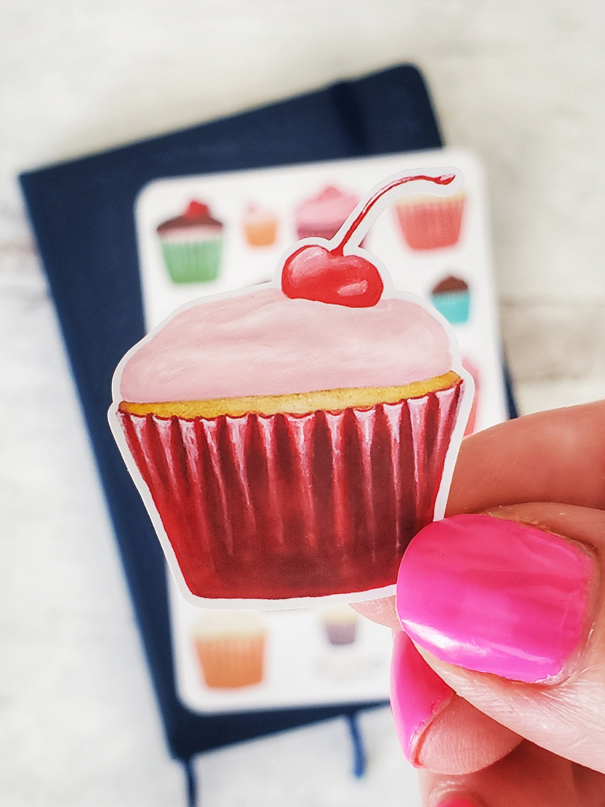 A close up of the cherry cupcake with pink frosting and a cherry on top.
