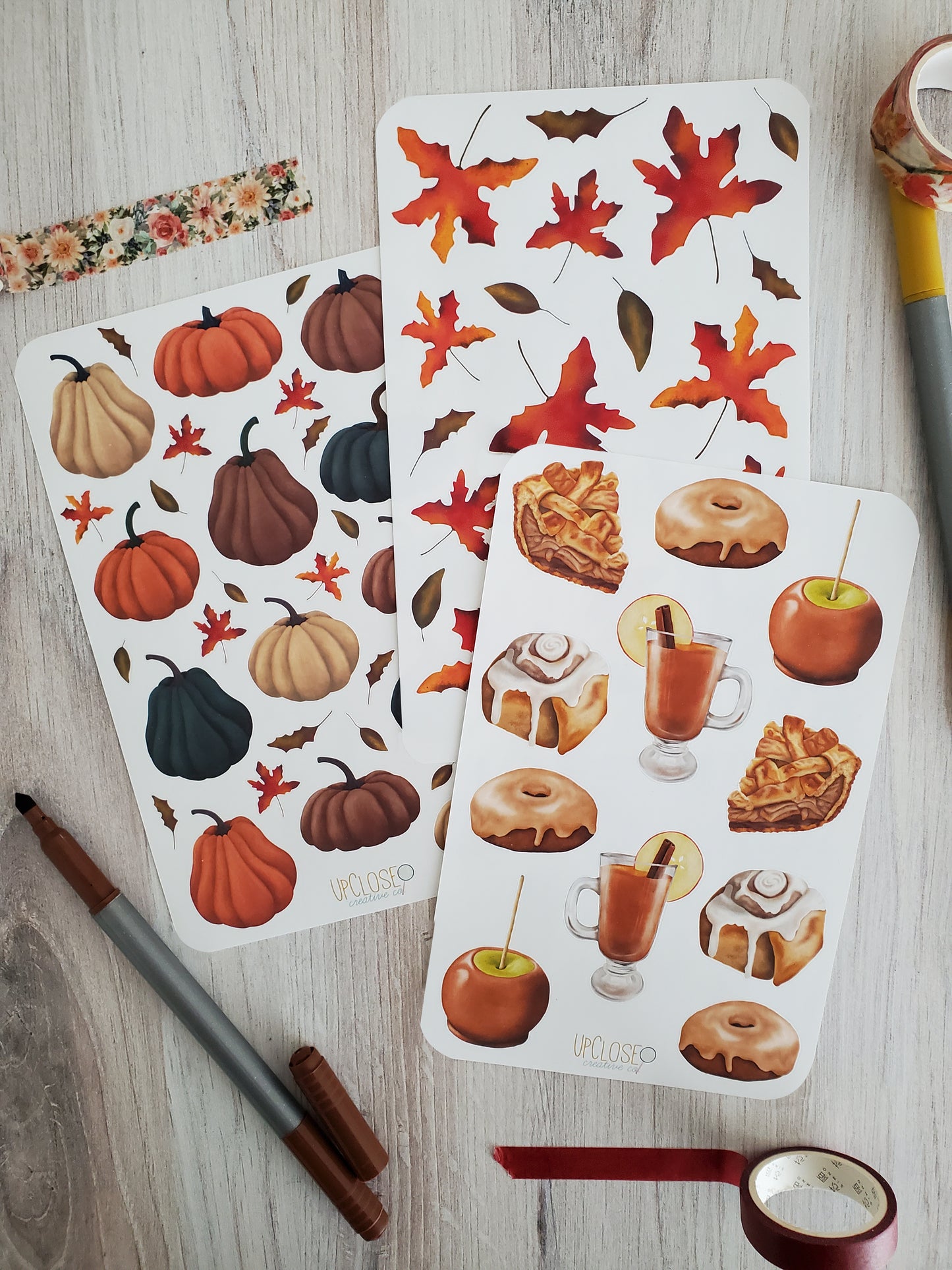 This bundle includes three sticker sheets. The first is pumpkins in deep hues of blue, orange, mauve and cream. The second is fall leaves in deep red, orange, and green. The third is various fall treats, apple pie, cinnamon rolls, maple doughnuts, apple cider and a caramel apple.