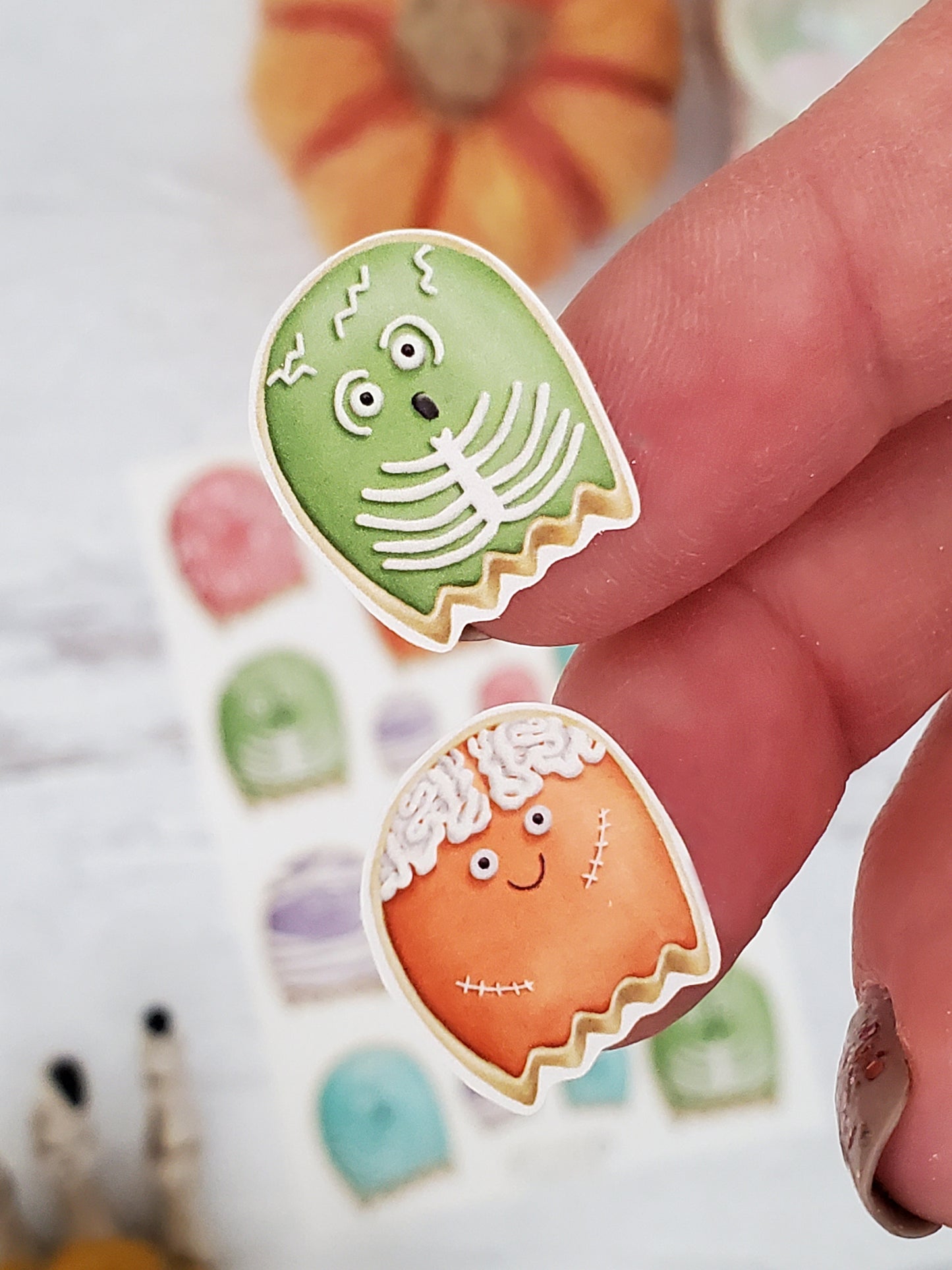 close up of two ghost cookie stickers, a green skeleton ghost and orange zombie ghost