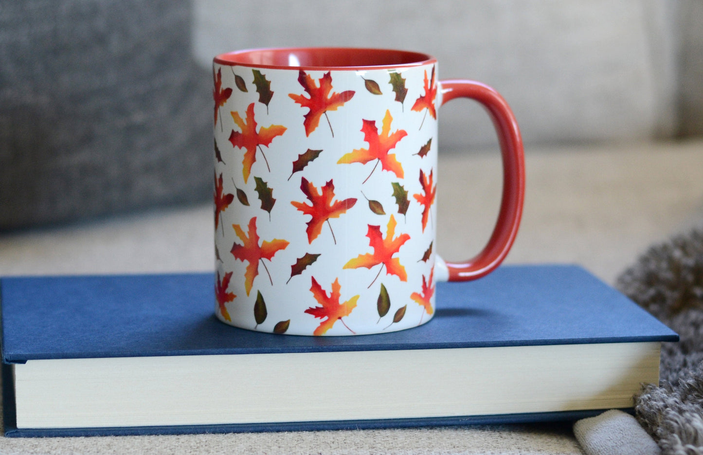 fall leaves mug sitting on a book with comfy couch in the background